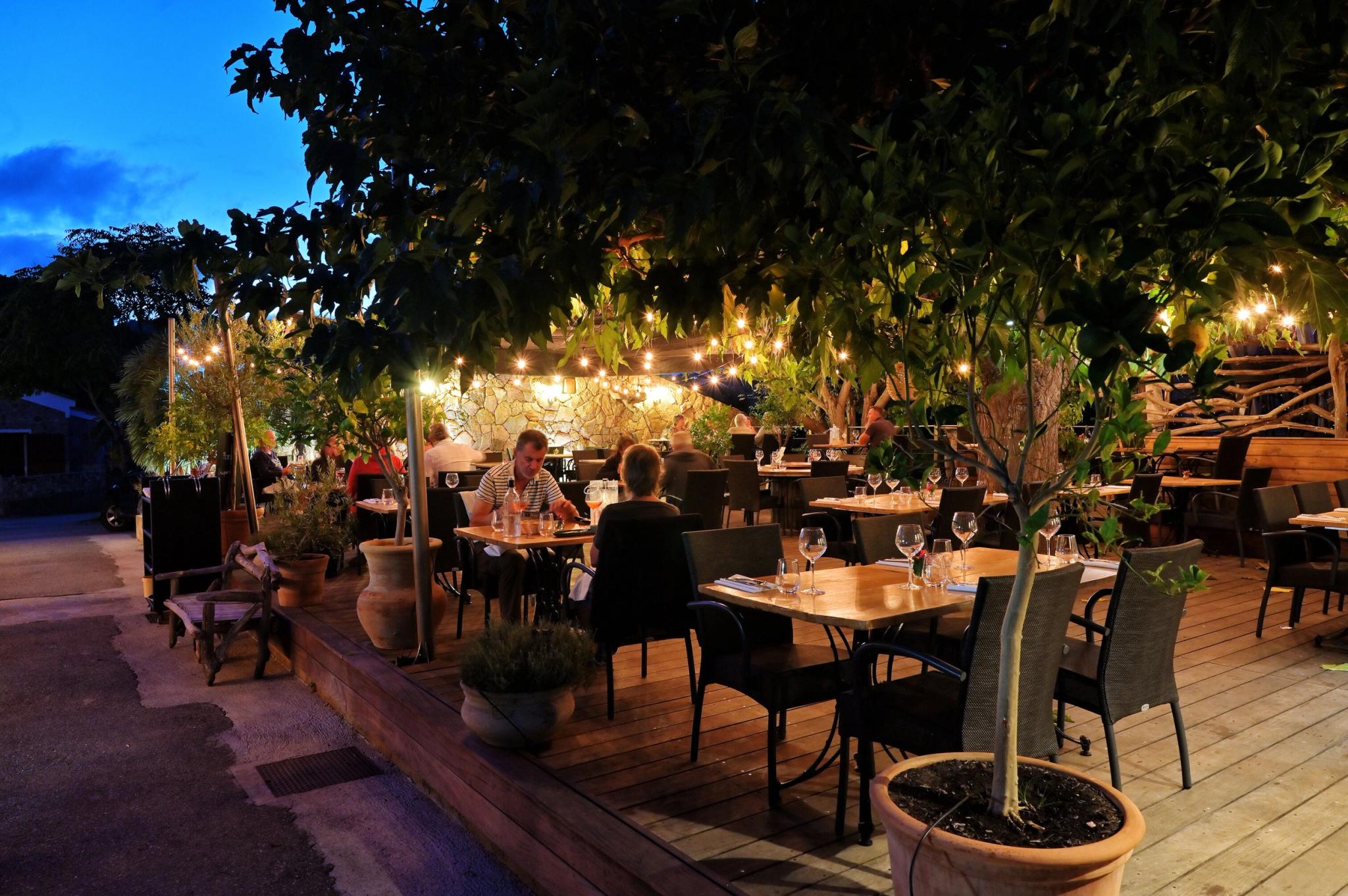 Restaurant corse en terrasse illuminée le soir avec tables dressées et décoration végétale